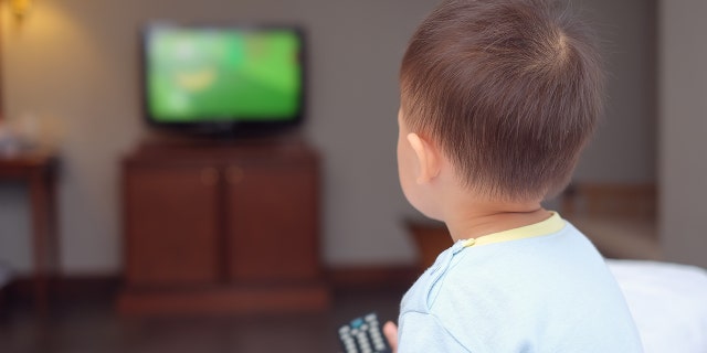 Toddler boy sitting in bed holding the tv remote control and watching television. (Photo: iStock)