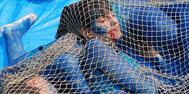 The dead-serious protesters laid on a blue tarp on the ground, with their tangled limbs painted blue, and blood-like red paint dripping from their mouths.