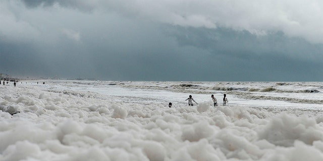 Residents play over foamy discharge, caused by pollutants, as it mixes with the surf at Marina beach in Chennai on December 1, 2019.