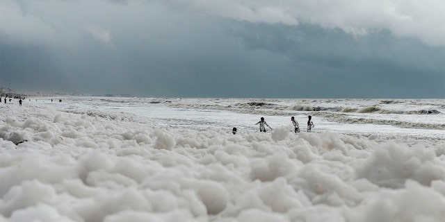 Residents play over foamy discharge, caused by pollutants, as it mixes with the surf at Marina beach in Chennai on December 1, 2019.