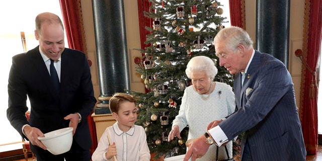 In this photo provided by Buckingham Palace, Britain's Queen Elizabeth, Prince Charles, Prince William and Prince George smile as they prepare special Christmas puddings in the Music Room at Buckingham Palace, London, as part of the launch of The Royal British Legion's Together at Christmas initiative.