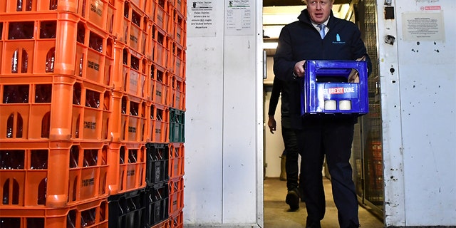 Britain's Prime Minister Boris Johnson carries a crate of milk bearing the Conservative Party campaign slogan at a milk delivery business. (AP)