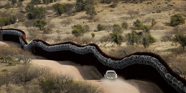A Customs and Border Control agent patrols on the US side of a razor-wire-covered border wall along the Mexico east of Nogales, Ariz.