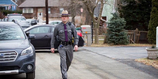 A New York state trooper walking past the house, with green siding, of the mother of Grafton Thomas, the primary suspect in the Saturday night stabbings at a rabbi's home in Monsey, N.Y. (AP)
