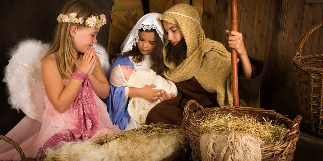 Little 7-year-old angel visiting a Nativity scene reenacted with a doll