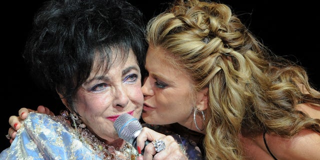 Model Kathy Ireland kisses Elizabeth Taylor during the 27th Annual Macy's Passport Fashion Show Benefit at Barker Hanger on September 24, 2009 in Santa Monica, California.