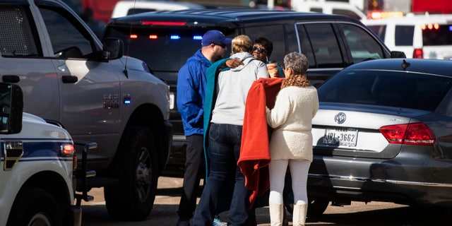 Residents embrace near police and fire cars that surround the scene of a shooting at West Freeway Church of Christ in White Settlement, Texas, Sunday, Dec. 29, 2019.