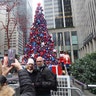 Two people have their pictures taken in front of the Christmas tree in FOX Square in New York City.