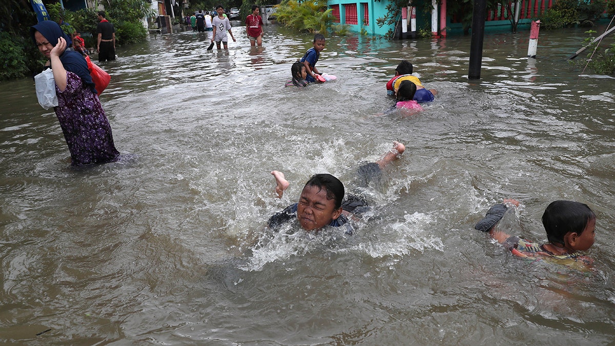 Children play in a flooded neighborhood in Tanggerang on the outskirts of Jakarta, Indonesia, Thursday, Jan. 2, 2020. Severe flooding in Indonesia's capital as residents celebrated the new year has killed at least 16 people, displaced tens of thousands and forced an airport to close, the country's disaster management agency said Thursday. (AP Photo/Tatan Syuflana)