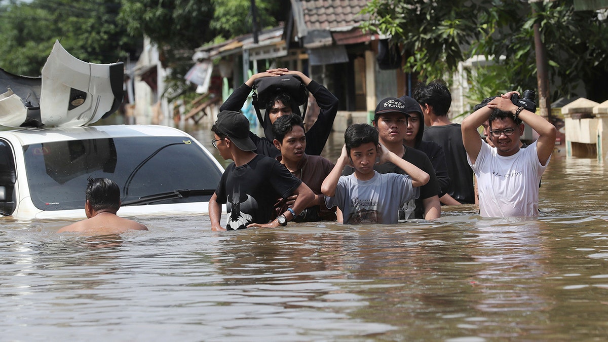 People walk through a flooded neighborhood in Tanggerang, outisde Jakarta, Indonesia, Thursday, Jan. 2, 2020. Heavy flooding in Indonesia's capital as residents celebrated the new year has killed scores of people, displaced tens of thousands and forced an airport to close, the country's disaster management agency said Thursday. (AP Photo/Tatan Syuflana)