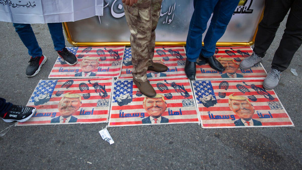 Mourners step over a U.S. flags with pictures of President Trump while waiting for the funeral of Iran's top general Qassem Soleimani and Abu Mahdi al-Muhandis, deputy commander of Iran-backed militias in Iraq known as the Popular Mobilization Forces, in Baghdad, Iraq, Saturday