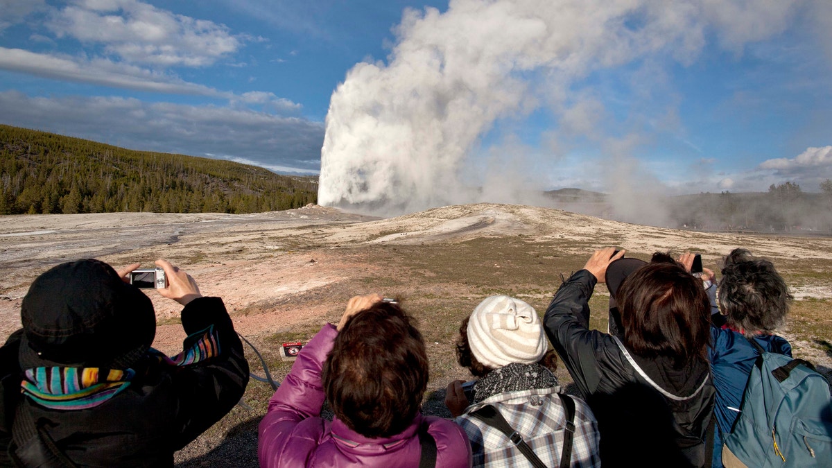 In this 2011, file photo, tourists photograph Old Faithful erupting on schedule late in the afternoon in Yellowstone National Park, Wyo. Two men who pleaded guilty to trespassing on the cone of Old Faithful Geyser in Yellowstone National Park were sentenced to 10 days in jail and have been banned from the park for five years. (AP Photo/Julie Jacobson, File)