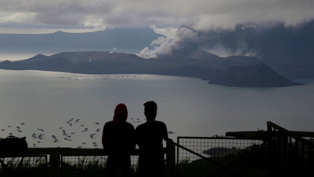 Men watch from Tagaytay, Cavite province, south of Manila, as Taal Volcano continues to spew ash on Tuesday, Jan. 14, 2020. Thousands of people fled the area through heavy ash as experts warned that the eruption could get worse and plans were being made to evacuate more.(AP Photo/Aaron Favila)