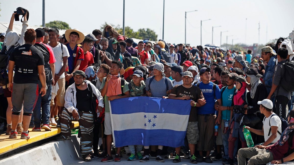 Central American migrants holding Honduras' national flag stand on the legal border crossing bridge over the Suchiate River that connects Tecun Uman, Guatemala with Ciudad Hidalgo in Mexico. (AP Photo/Moises Castillo)