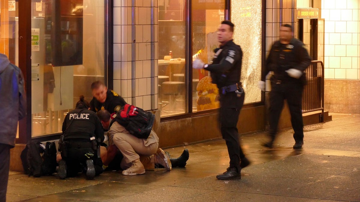Officers attend to one of several shooting victims, outside of a McDonald's on Seattle's Third Avenue. The window of the restaurant behind them was shattered after a gunman opened fire in the heavily trafficked downtown area. (David Silver via AP)