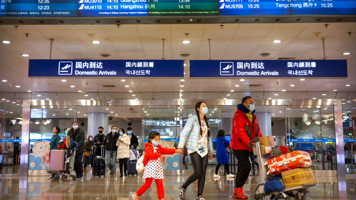 Travelers in face masks walk past a display board showing a canceled flight from Wuhan at Beijing Capital International Airport in Beijing.