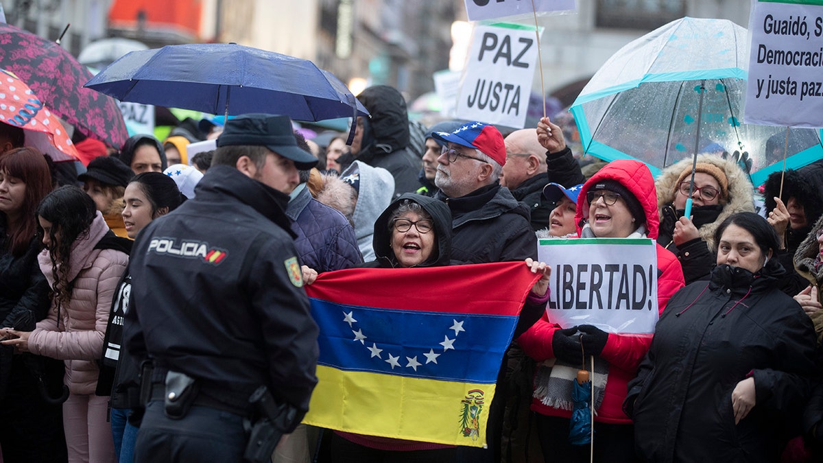 A woman holds a Venezuelan flag as others pack the Puerta del Sol square waiting for Juan Guaido during his visit to Madrid, Spain, Saturday, Jan. 25, 2020. Juan Guaido, the man who one year ago launched a bid to oust Venezuelan President Nicolas Maduro, arrived Saturday in Spain, where a thriving community of Venezuelans and a storm among Spanish political parties awaited him. Banners read 'Peace and6Freedom' (AP Photo/Paul White)