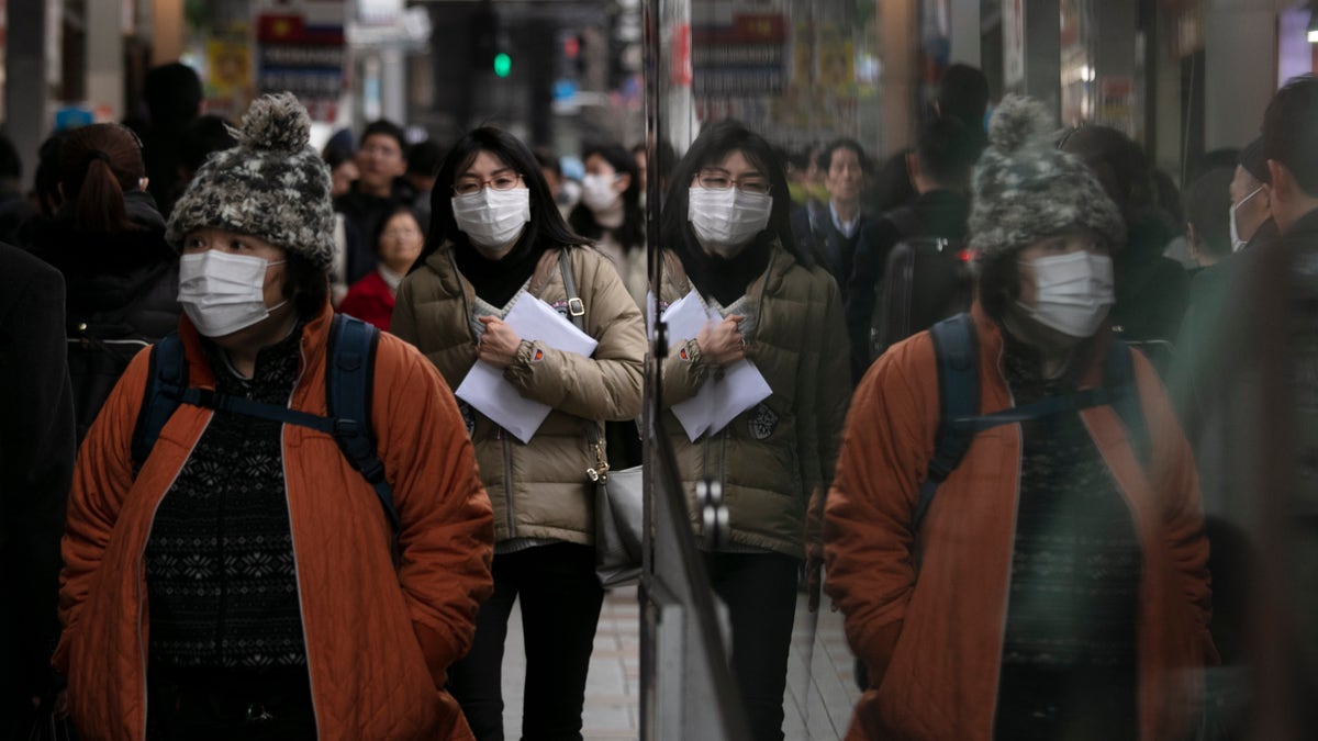Commuters wearing protective face masks walk on a sidewalk Monday, Jan. 27, 2020, in the Shinjuku district of Tokyo. China has extended its Lunar New Year holiday three more days to discourage people from traveling as it tries to contain the spread of a viral illness that has caused dozens of deaths. (AP Photo/Jae C. Hong)