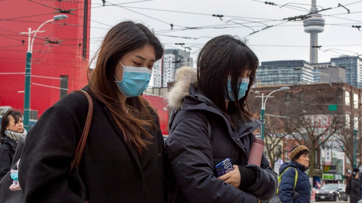 Pedestrians wear protective masks as they walk in Toronto on Monday. Canada's first presumptive case of the novel coronavirus has been officially confirmed, Ontario health officials said Monday as they announced the patient's wife has also contracted the illness. Surgical-style masks at U.S. pharmacies have reportedly begun selling out in several cities amid fears of the virus. (Frank Gunn/The Canadian Press via AP)