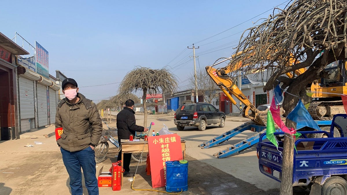 A man wearing a face mask stands near a barricade at the entrance to Donggouhe village in northern China's Hebei Province on Wednesday. With barricades and wary guardians, villages on the outskirts of Beijing are closing themselves off to outsiders to ward against infection amid the outbreak of a new type of virus. (AP Photo)