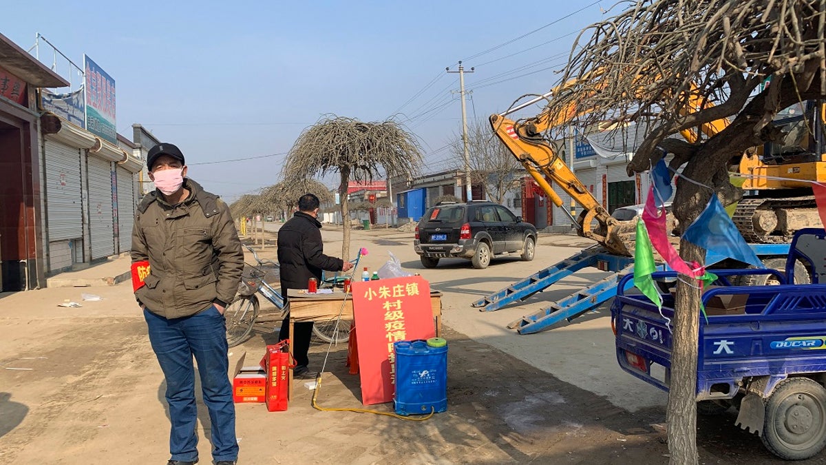 A man wearing a face mask stands near a barricade at the entrance to Donggouhe village in northern China's Hebei Province on Wednesday. With barricades and wary guardians, villages on the outskirts of Beijing are closing themselves off to outsiders to ward against infection amid the outbreak of a new type of virus. (AP Photo)