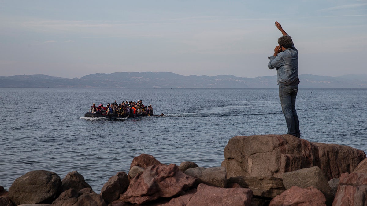 In this Wednesday, Sept. 9, 2015 photo refugees and migrants aboard an overcrowded dinghy as they cross the Aegean Sea, from Turkey, that is seen in the background, to the coast of Lesbos island, Greece.  (AP Photo/Petros Giannakouris)