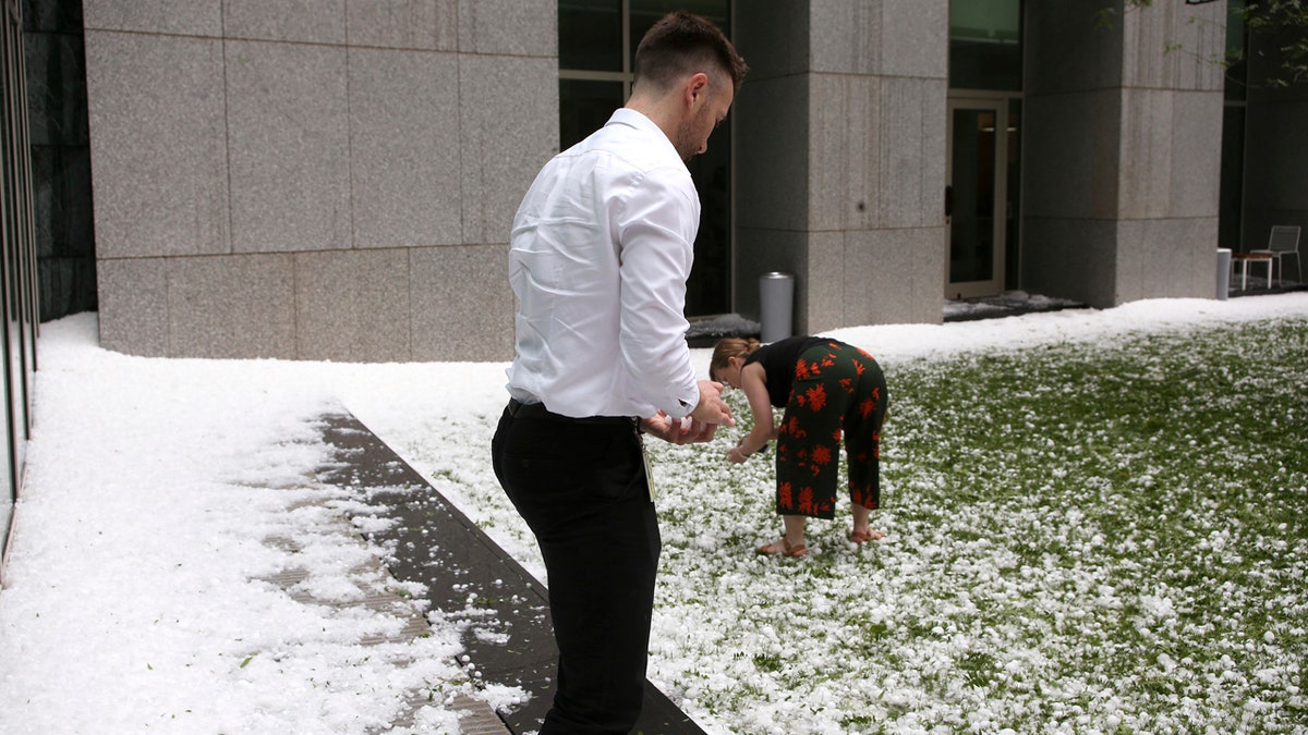 A man and woman collect golfball-sized hail on the grounds of Parliament House in Canberra, Australia, after a storm battered the Australian capital, Monday, Jan. 20, 2020.