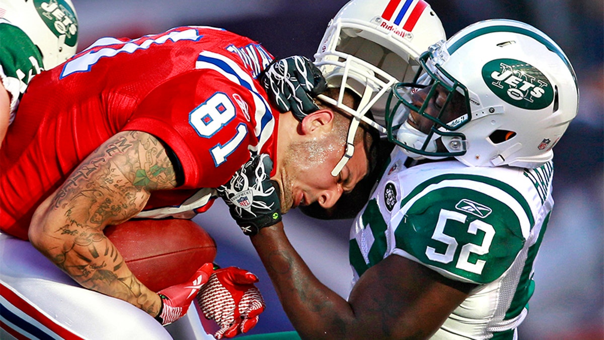 New England Patriots tight end Aaron Hernandez (81) hangs on to the ball as New York Jets inside linebacker David Harris (52) takes off his helmet on a hit during the first half of an NFL football game in Foxborough, Mass., Sunday, Oct. 9, 2011.