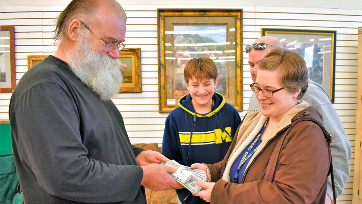 In this Jan. 16, 2020 photo, Howard Kirby, left, gives $43,170 to Kim Fauth-Newberry at a resale store in Owosso Township, Mich.. Kirby's daughter-in-law found the money in a footstool that was donated to the store by Fauth-Newberry. The footstool had belonged to her grandfather, who died last summer. Kirby bought it along with other furniture after Christmas. (Sally York/The Argus-Press via AP)