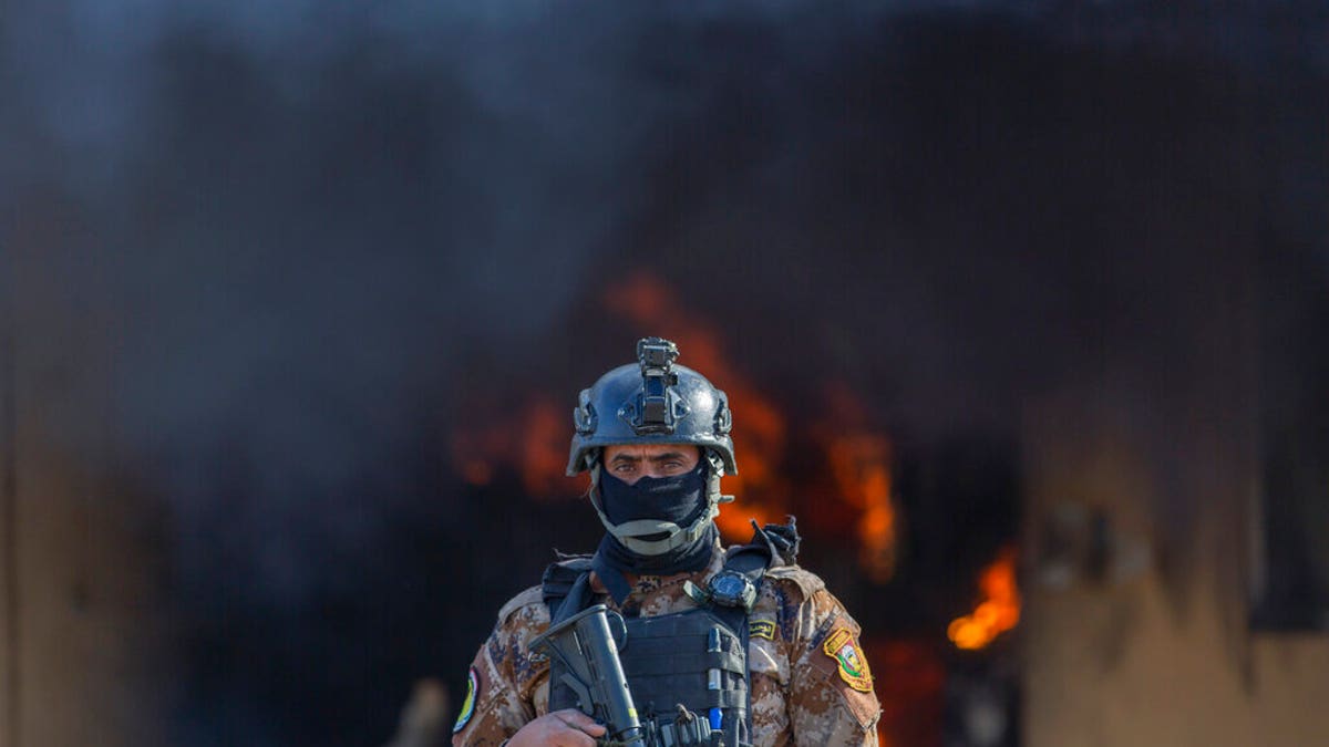 An Iraqi soldier stands guard in front of smoke rising from a fire set by pro-Iranian militiamen and their supporters in the U.S. embassy compound, Baghdad, Iraq, Wednesday, Jan. 1, 2020. (AP Photo/Nasser Nasser)
