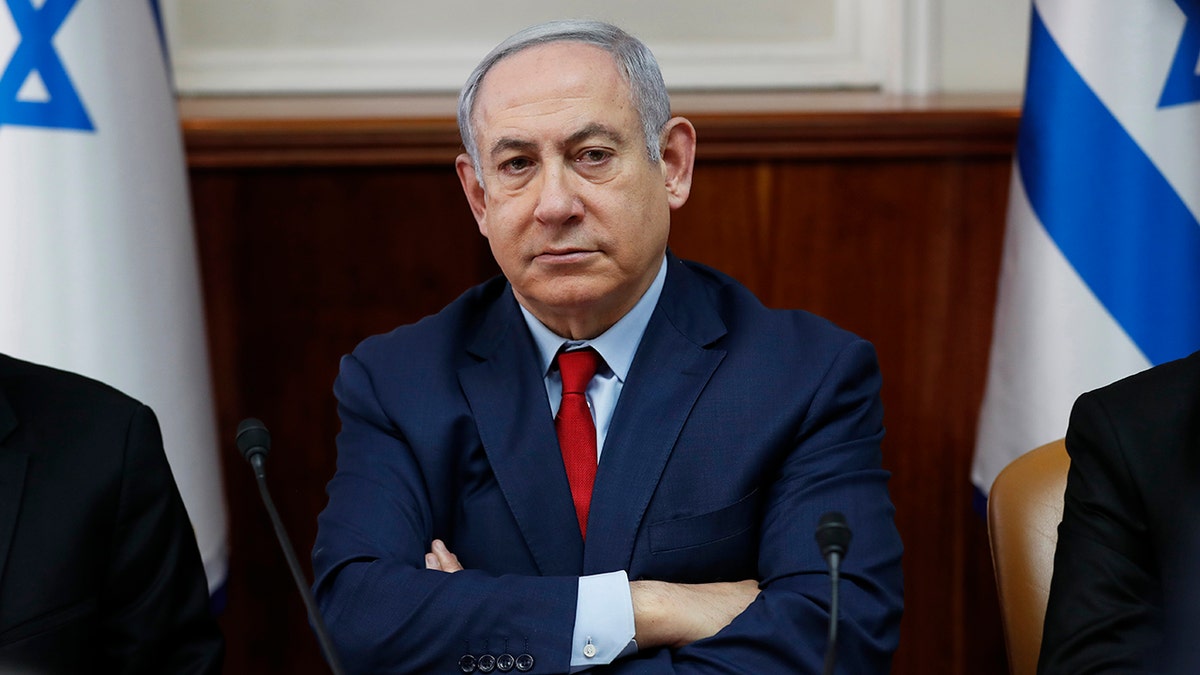 Benjamin Netanyahu in a suit between flags of Israel