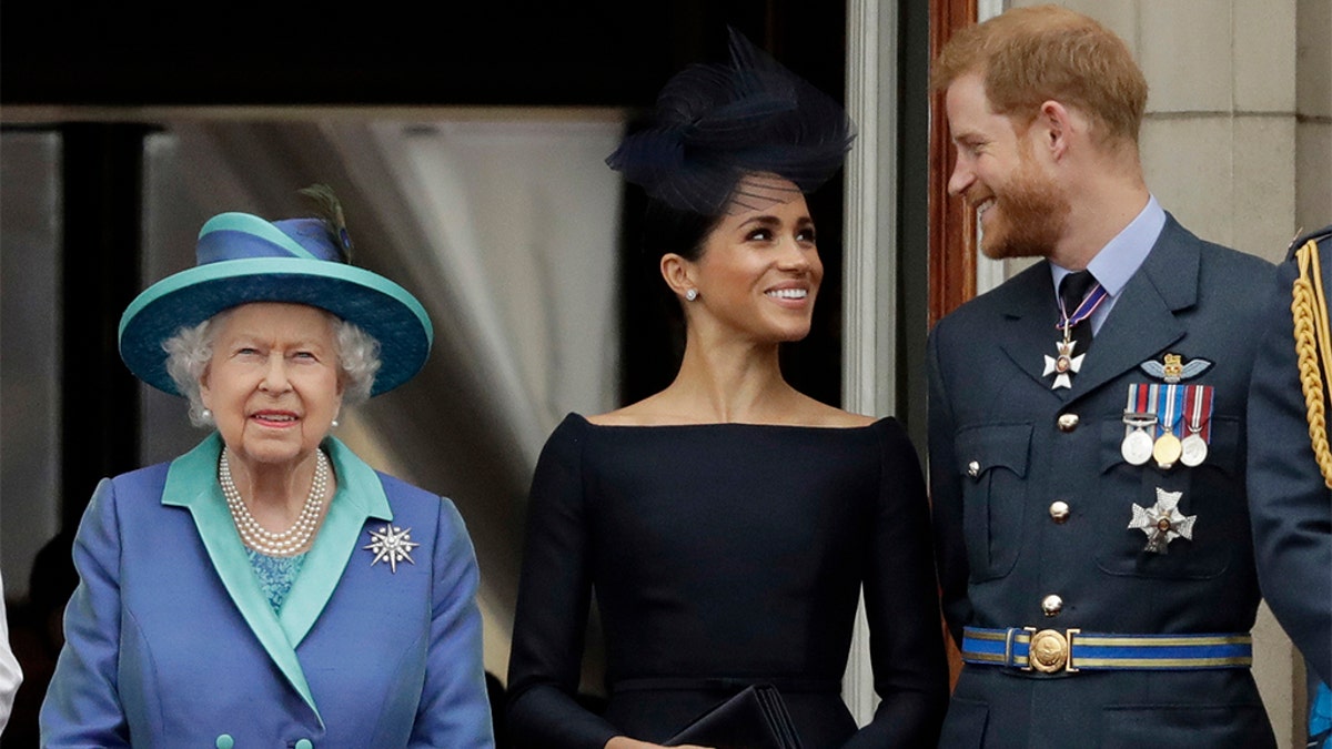 In this Tuesday, July 10, 2018 file photo, Britain's Queen Elizabeth II, and Meghan the Duchess of Sussex and Prince Harry watch a flypast of Royal Air Force aircraft pass over Buckingham Palace in London. 
