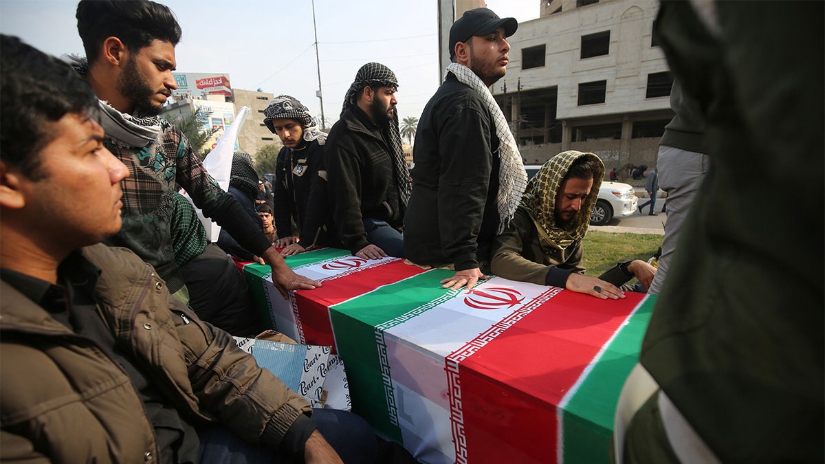 Iraqis surround a coffin, draped in an Iranian national flag, during the funeral procession of Iraqi paramilitary chief Abu Mahdi al-Muhandis, Iranian military commander Qasem Soleimani, and eight others, in the capital Baghdad's district of al-Jadriya, near the high-security Green Zone, on January 4, 2020.