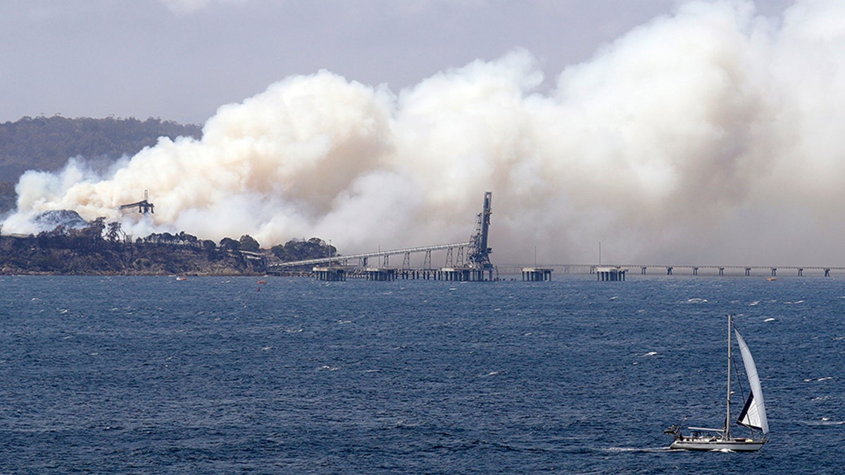 A yacht sails past a burning woodchip mill as the wildfires hit the town of Eden, New South Wales, Australia, on Friday. (AP)