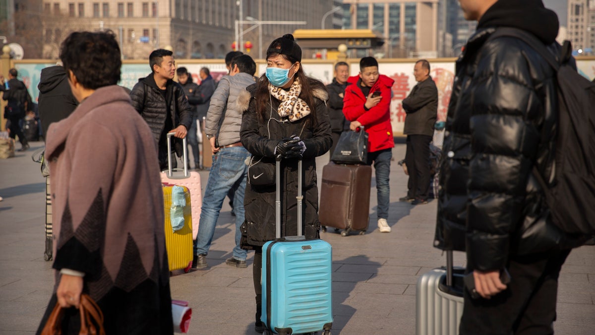 A traveler wears a face mask as she stands near the Beijing Railway Station in Beijing.