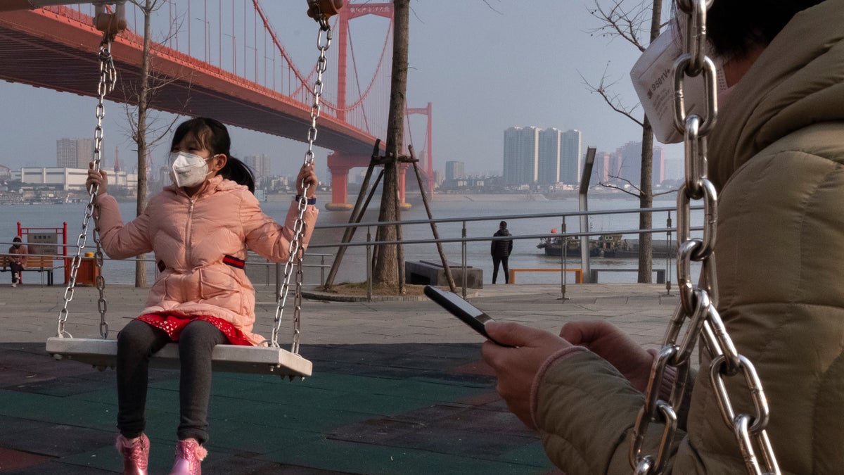 A girl wears a face mask as she play on a swing near the Yingwuzhou Yangtze River Bridge in Wuhan in central China's Hubei Province, Wednesday, Jan. 29, 2020. Countries began evacuating their citizens Wednesday from the Chinese city hardest-hit by a new virus that has now infected more people in China than were sickened in the country by SARS. (AP Photo/Arek Rataj)