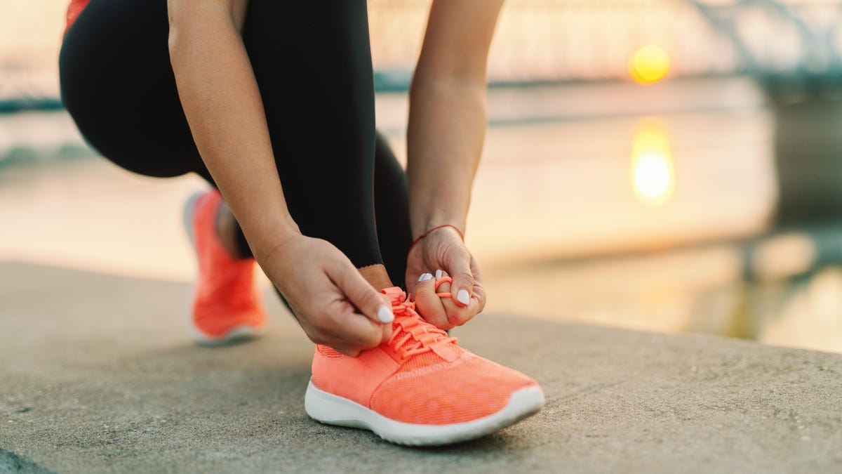 Close up of sporty woman tying shoelace while kneeling outdoor, In background bridge. Fitness outdoors concept.