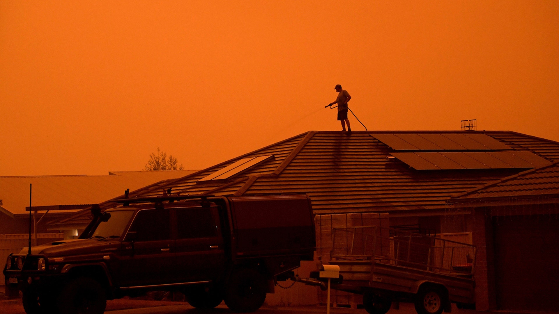A resident uses a garden hose to wet down their house as high winds push smoke and ash from the Currowan Fire towards Nowra, New South Wales, Australia Jan 4, 2020.
