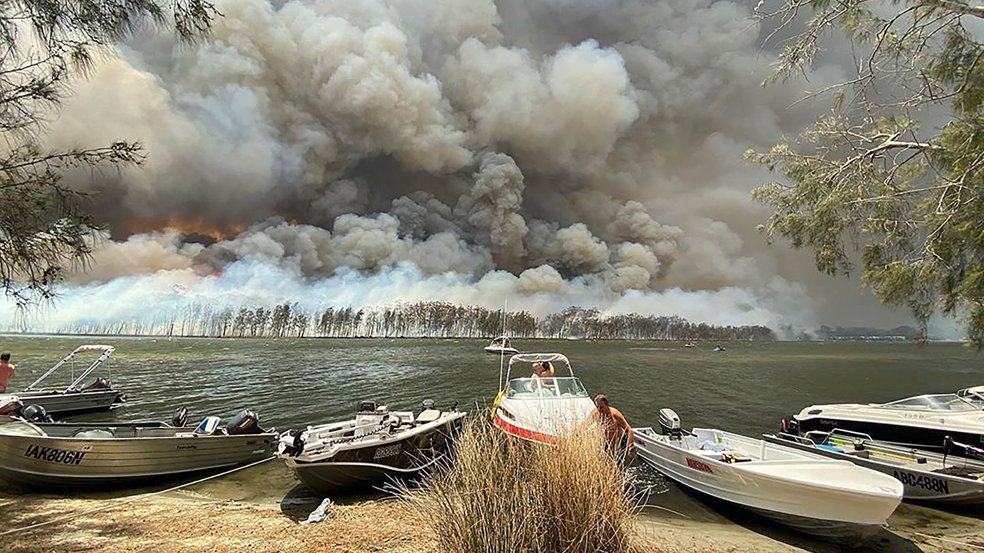 Boats are pulled ashore as smoke and wildfires rage behind Lake Conjola, Australia, Jan. 2, 2020.