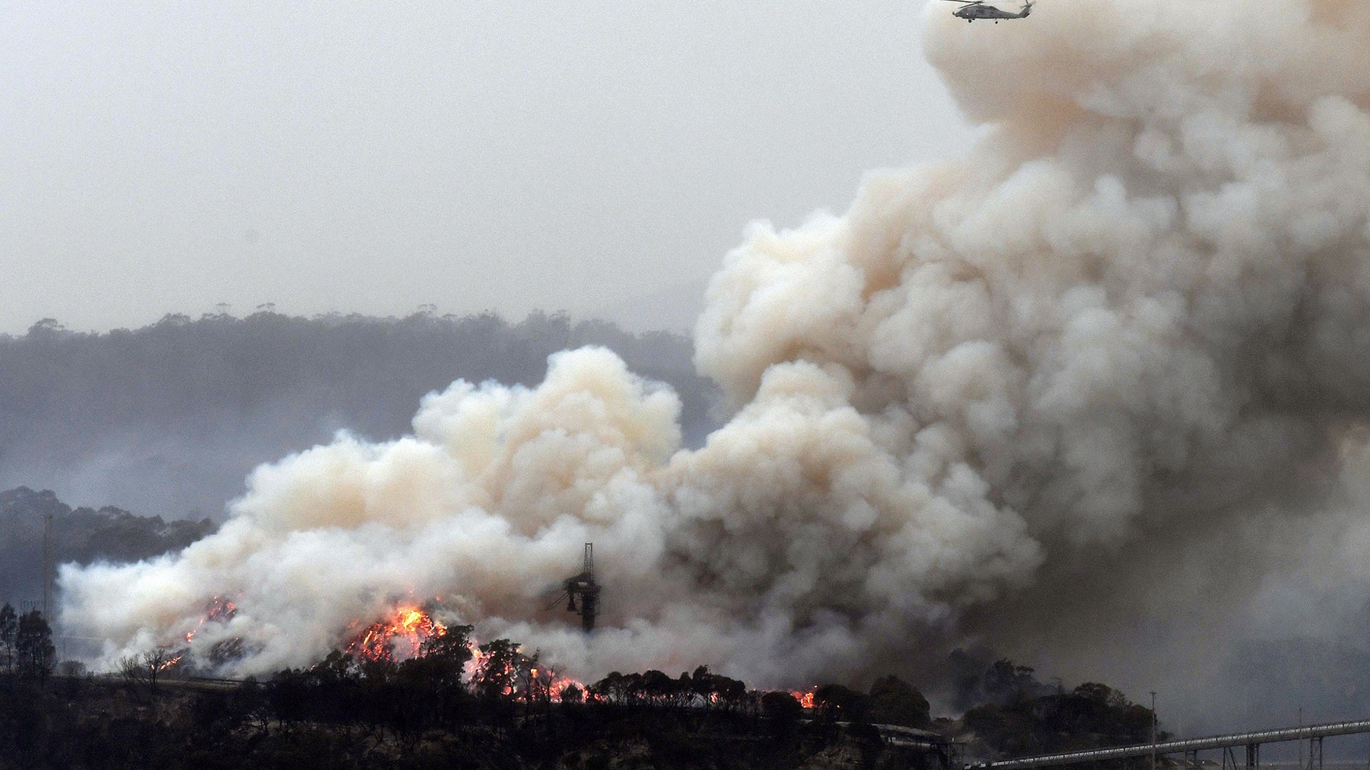 A military helicopter flies above a burning woodchip mill in Eden, New South Wales, Jan 6, 2020.