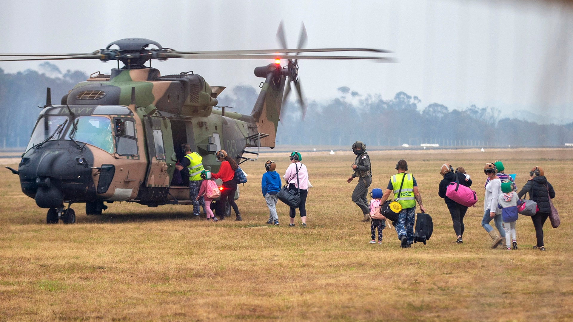People walk to board a helicopter as they are evacuated from the community of Mallacoota, Jan. 5, 2020.