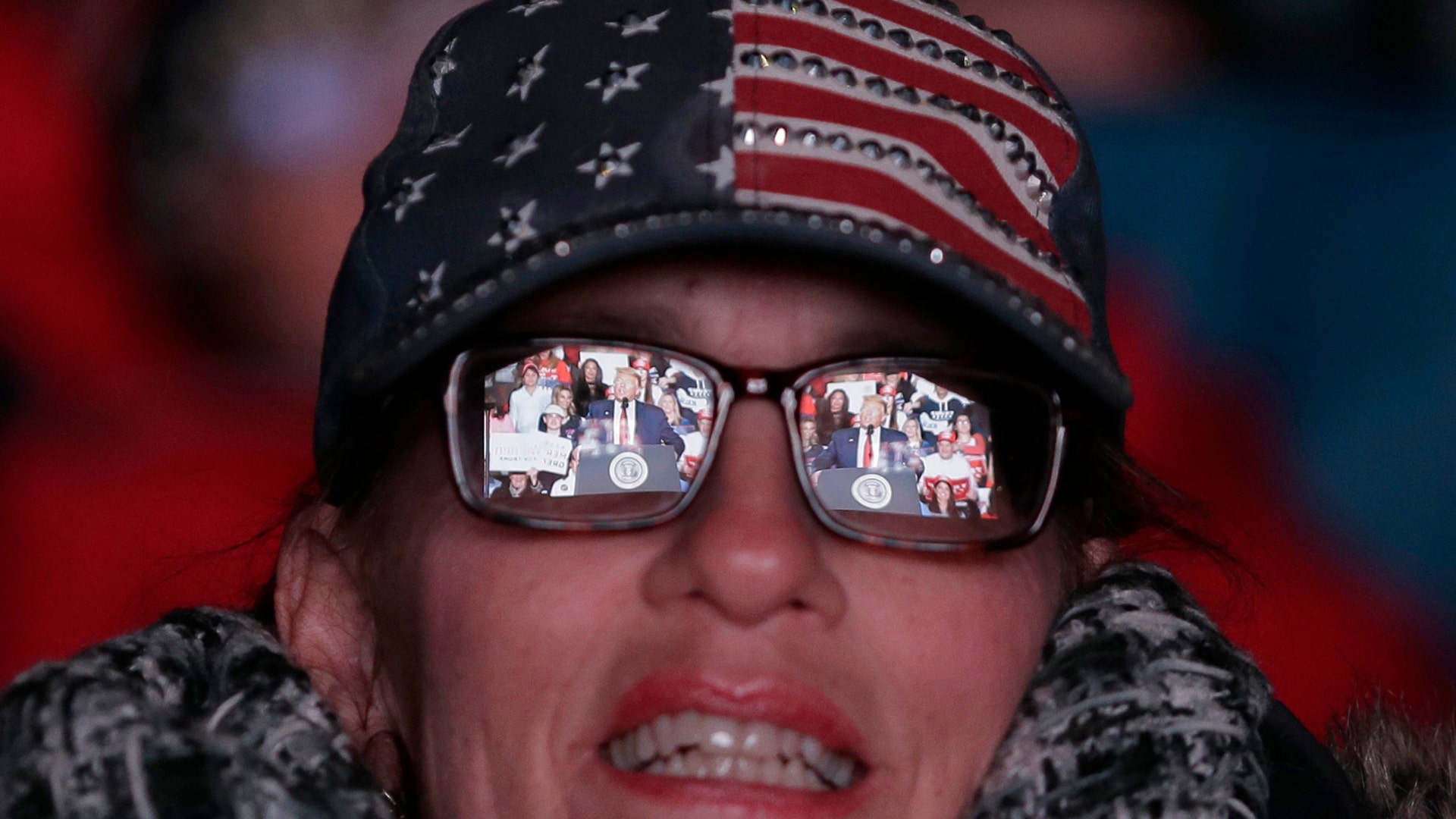 A large screen displaying President Donald Trump speaking is reflected in a woman's glasses outside a rally in Wildwood, New Jersey, Jan. 28, 2020.