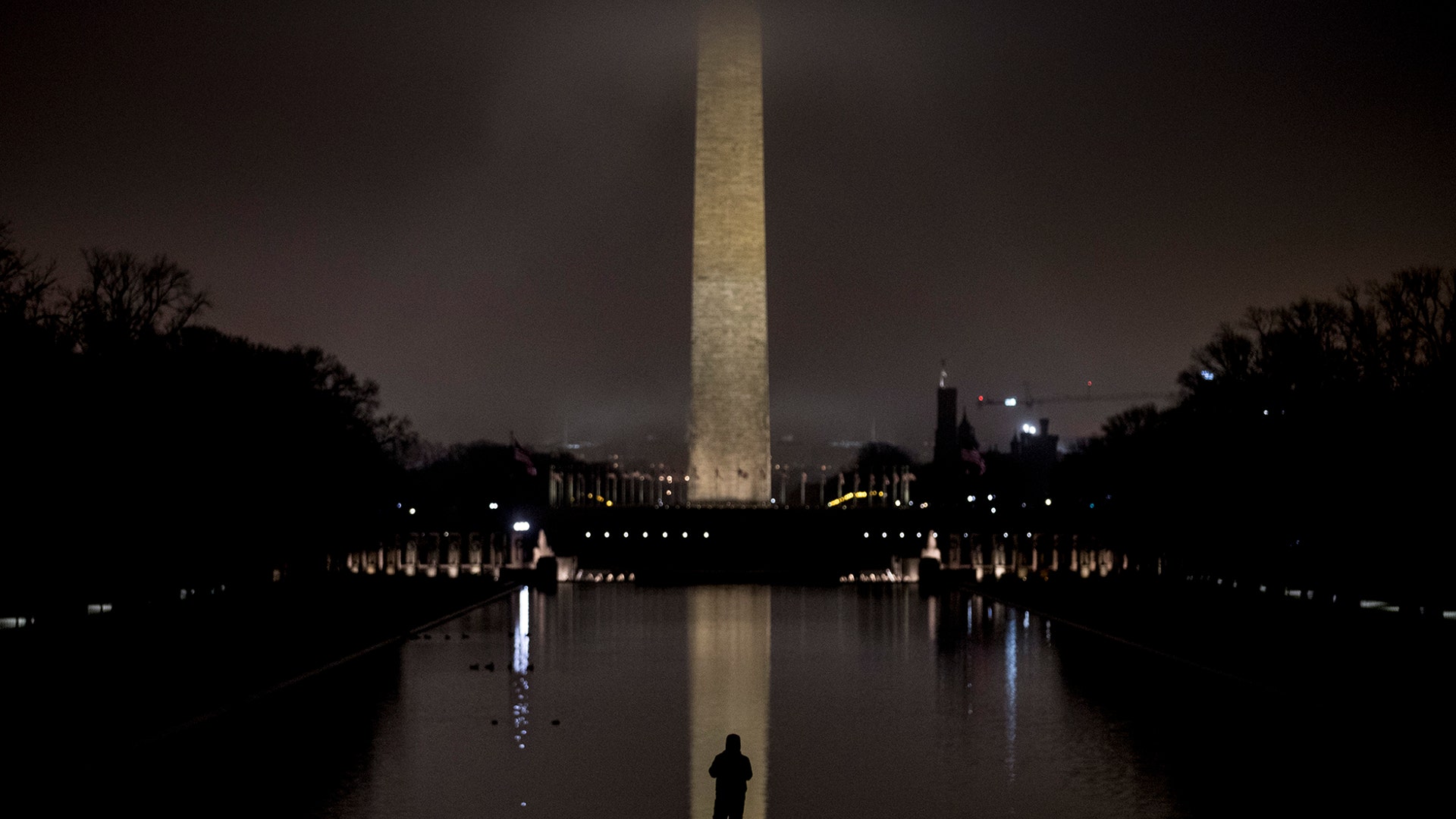 The Washington Monument, partially obscured by late evening fog, is visible as a man stands at the Reflecting Pool in Washington, Dec. 29, 2019.