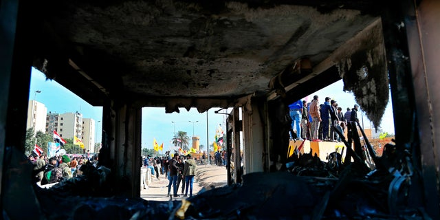 Pro-Iranian militiamen and their supporters are seen through broken windows of a burned checkpoint in front of the U.S. Embassy in Baghdad, Iraq, Wednesday, Jan. 1, 2020. (Associated Press)