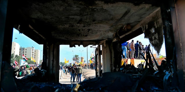 Pro-Iranian militiamen and their supporters are seen through broken windows of a burned checkpoint in front of the U.S. embassy in Baghdad, Iraq, Wednesday, Jan. 1, 2020. U.S. troops have fired tear gas to disperse hundreds of pro-Iran militiamen and other protesters who were gathered for a second day outside the American Embassy compound in Baghdad. (AP Photo/Khalid Mohammed)