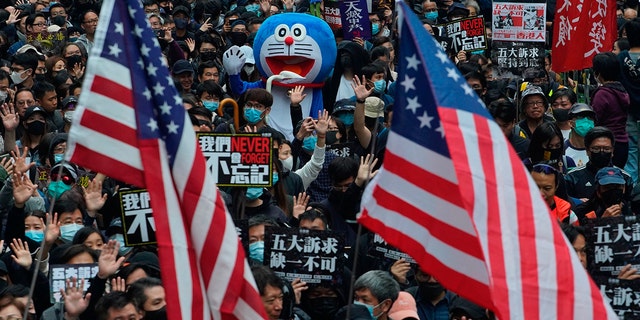 Hong Kong people wave the U.S flags and display a model of Doraemon during their annual pro-democracy march on New Year's Day to insist their five demands be matched by the government in Hong Kong, Wednesday, Jan. 1, 2020. The five demands include democratic elections for Hong Kong's leader and legislature and a demand for a probe of police behavior during the six months of continuous protests. (AP Photo/Vincent Yu)