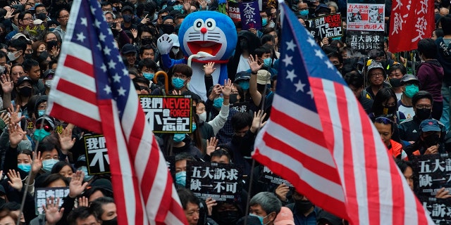 Hong Kong people wave the U.S flags and display a model of Doraemon during their annual pro-democracy march on New Year's Day to insist their five demands be matched by the government in Hong Kong, Wednesday, Jan. 1, 2020. The five demands include democratic elections for Hong Kong's leader and legislature and a demand for a probe of police behavior during the six months of continuous protests. (AP Photo/Vincent Yu)