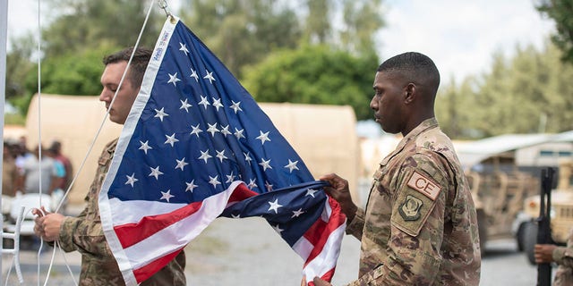 U.S. Air Force Staff Sgt. Sidney Dellinger and Staff Sgt. Corey Smith perform flag detail during a ceremony signifying the change from tactical to enduring operations at Camp Simba, Manda Bay, Kenya.