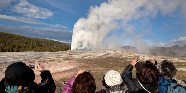 In this 2011, file photo, tourists photograph Old Faithful erupting on schedule late in the afternoon in Yellowstone National Park, Wyo. Two men who pleaded guilty to trespassing on the cone of Old Faithful Geyser in Yellowstone National Park were sentenced to 10 days in jail and have been banned from the park for five years. (AP Photo/Julie Jacobson, File)