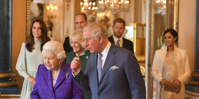 Britain's Queen Elizabeth II is joined by Prince Charles, the Prince of Wales, and at rear, from left, Kate, Duchess of Cambridge, Camilla, Duchess of Cornwall, Prince William, Prince Harry and Meghan, Duchess of Sussex during a reception at Buckingham Palace, London to mark the 50th anniversary of the investiture of the Prince of Wales. 
